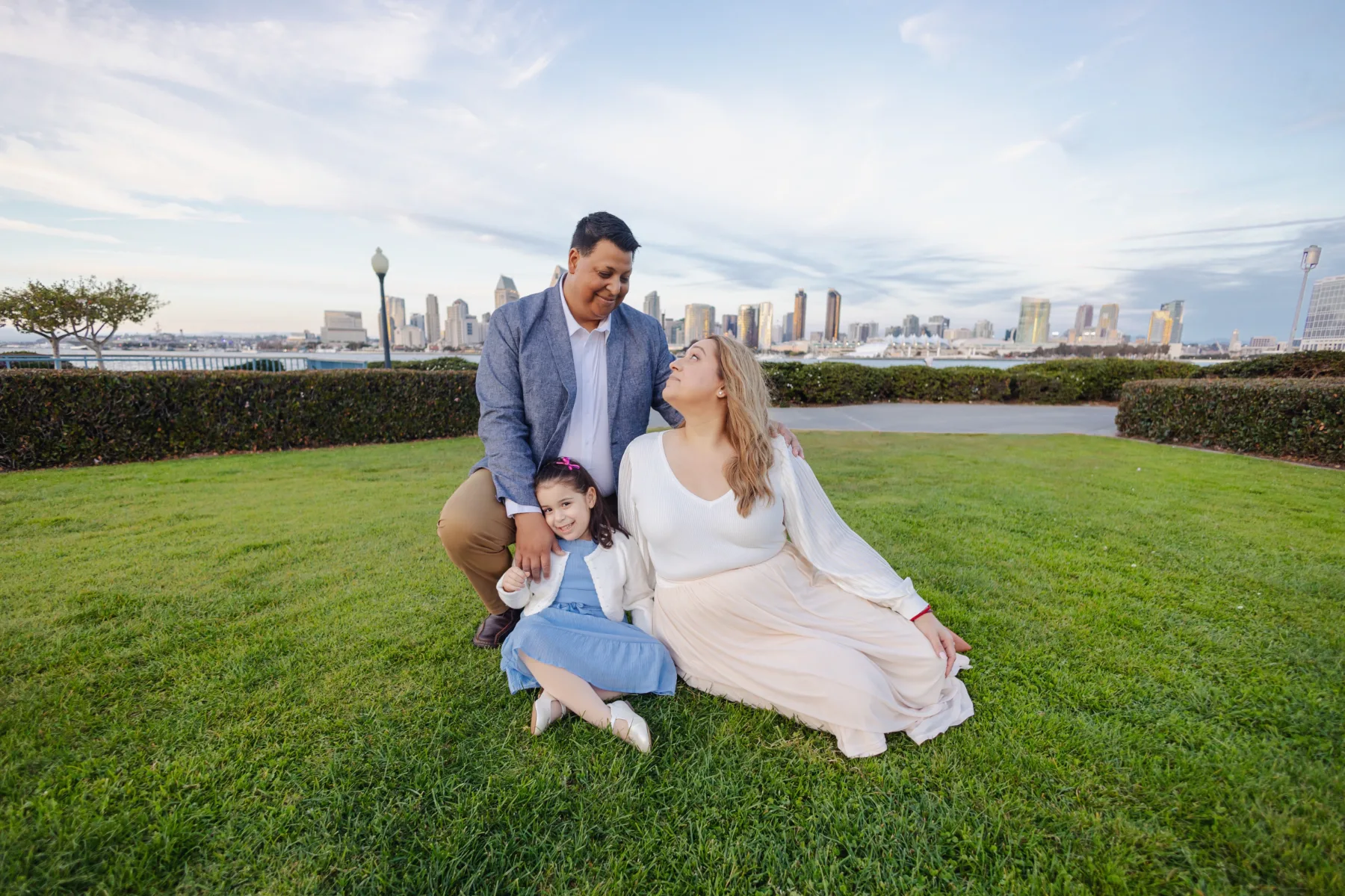Mom, dad and daughter sitting on the grass with the San Diego skyline, JSOLOVISUALS