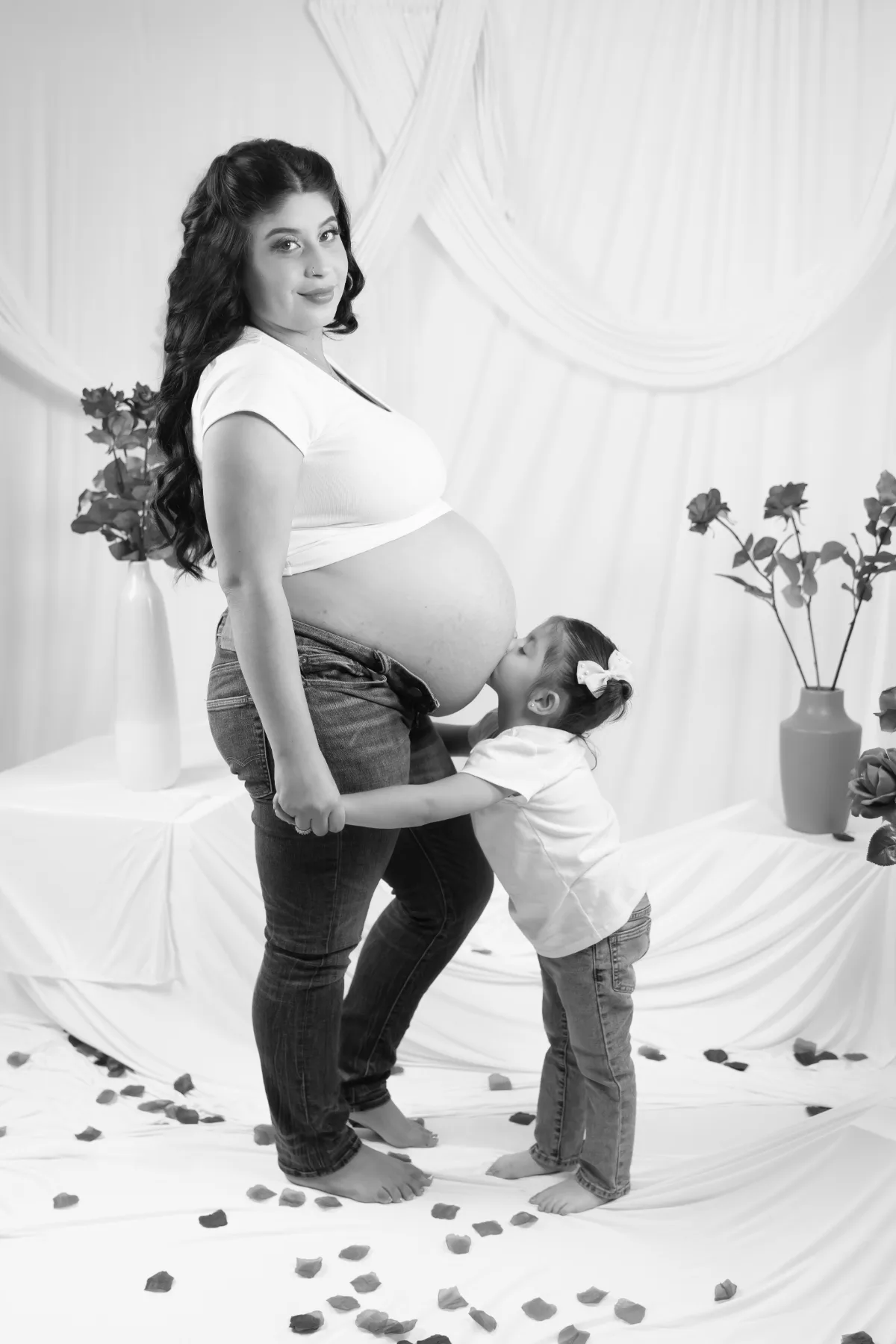 Black and white maternity portrait of a daughter kissing mom's belly in the studio