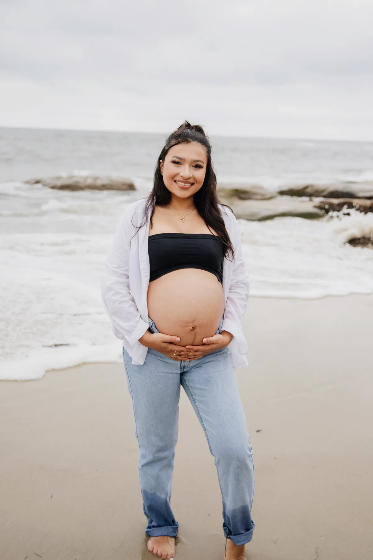 Smiling maternity portrait on the beach in jeans and a white shirt